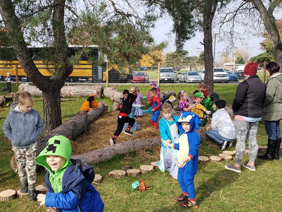 Children in halloween costumes play in an enfenced straw playground area
