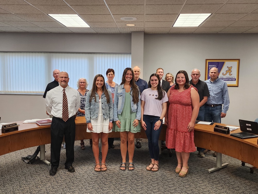 Students and staff stand gathered at a horshoe table