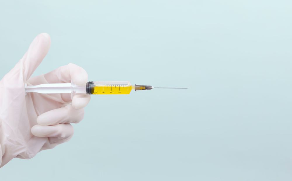 A gloved hand holding a syringe of yellow liquid