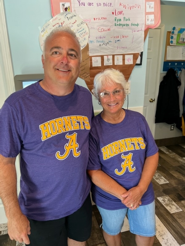 A man and a woman in purple and gold Angola hornets t-shirts pose and smile