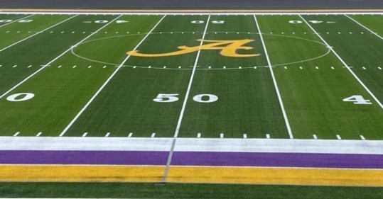 Turf football field, purple and gold sideline and a gold A in the center