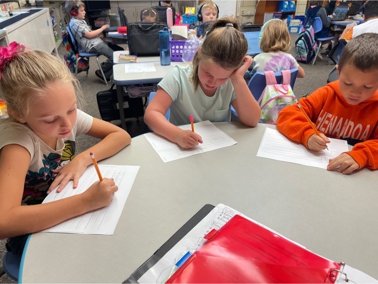 Students sitting in a small group writing words on paper with a pencil  