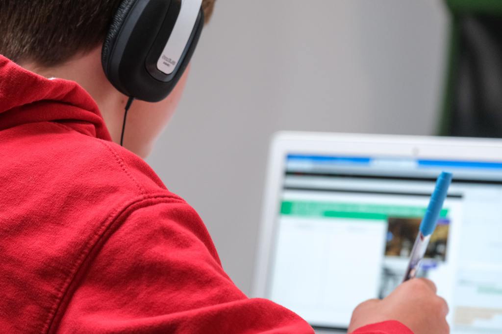 A boy in a red hoodie and headphones works on a computer